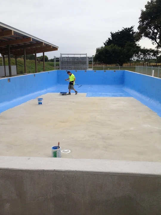Worker applying a coating to an empty outdoor swimming pool